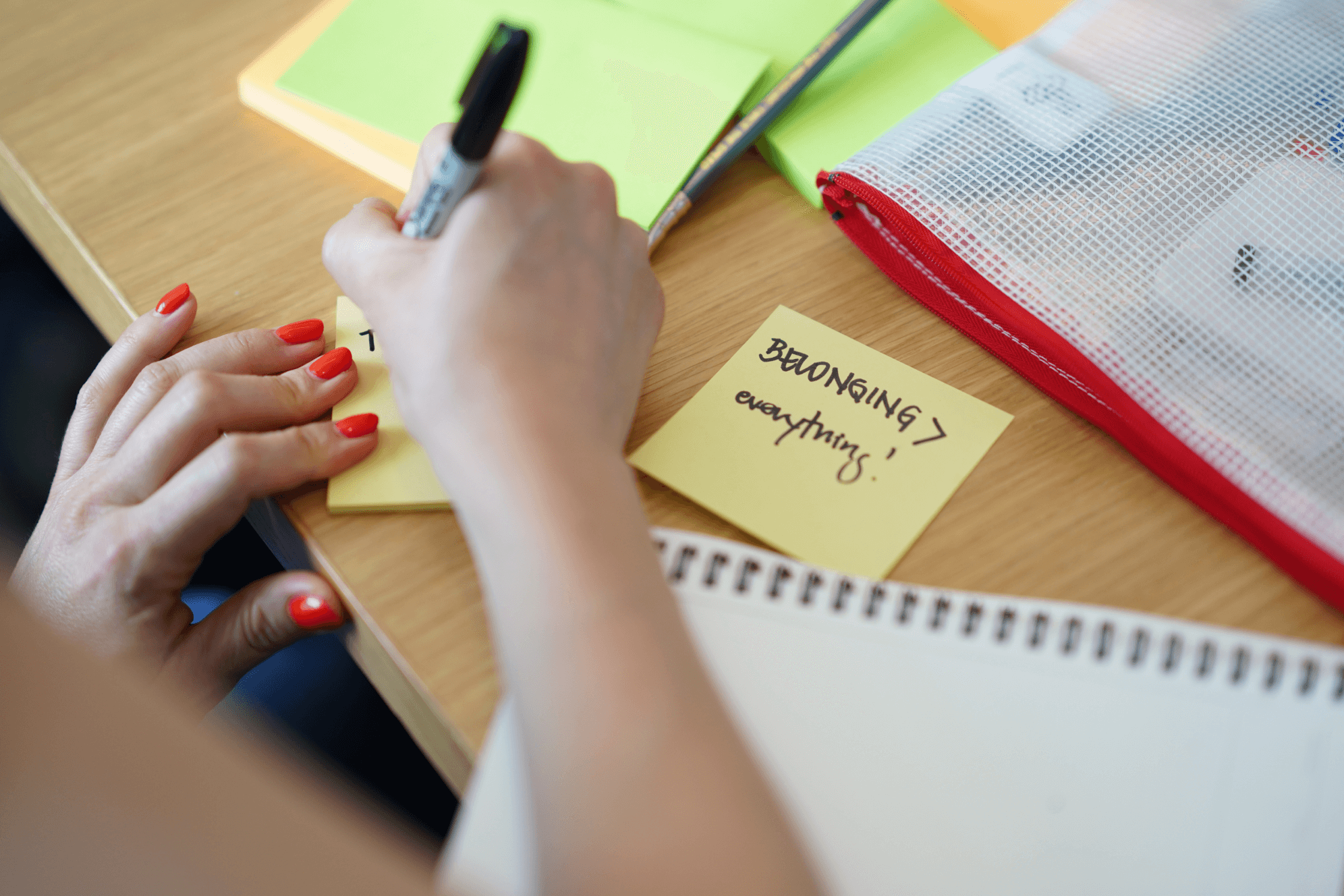 A close-up of a person's hands writing on a yellow sticky note with a black marker.